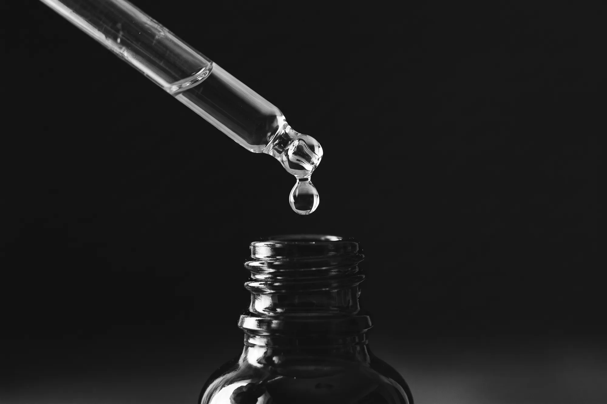 Conta-gotas soltando uma gota de essência em um frasco pequeno, em preto e branco