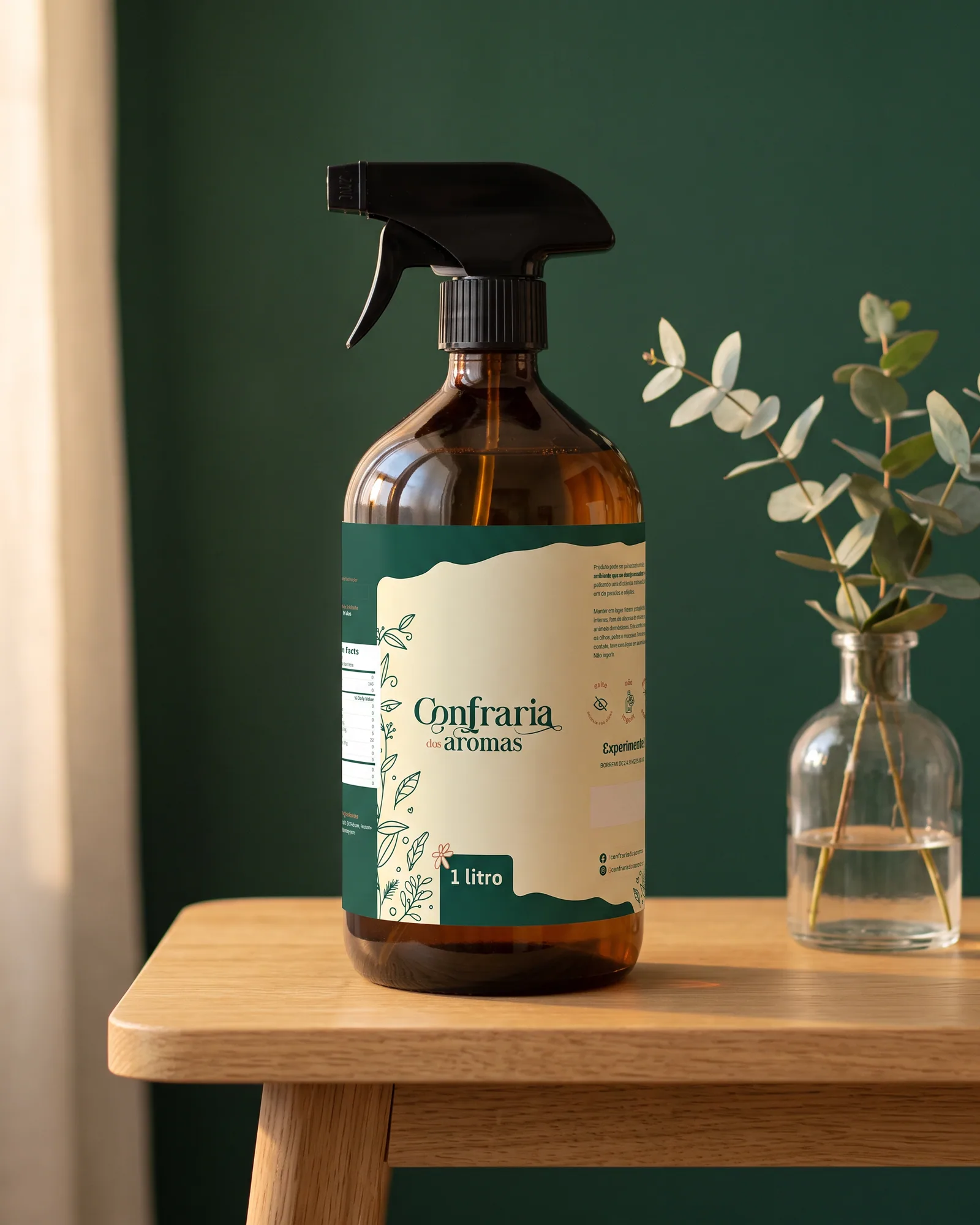 Frasco âmbar de aromatizador de ambiente de 1 litro com o rótulo da Confraria dos Aromas, ao lado de um vaso com eucalipto