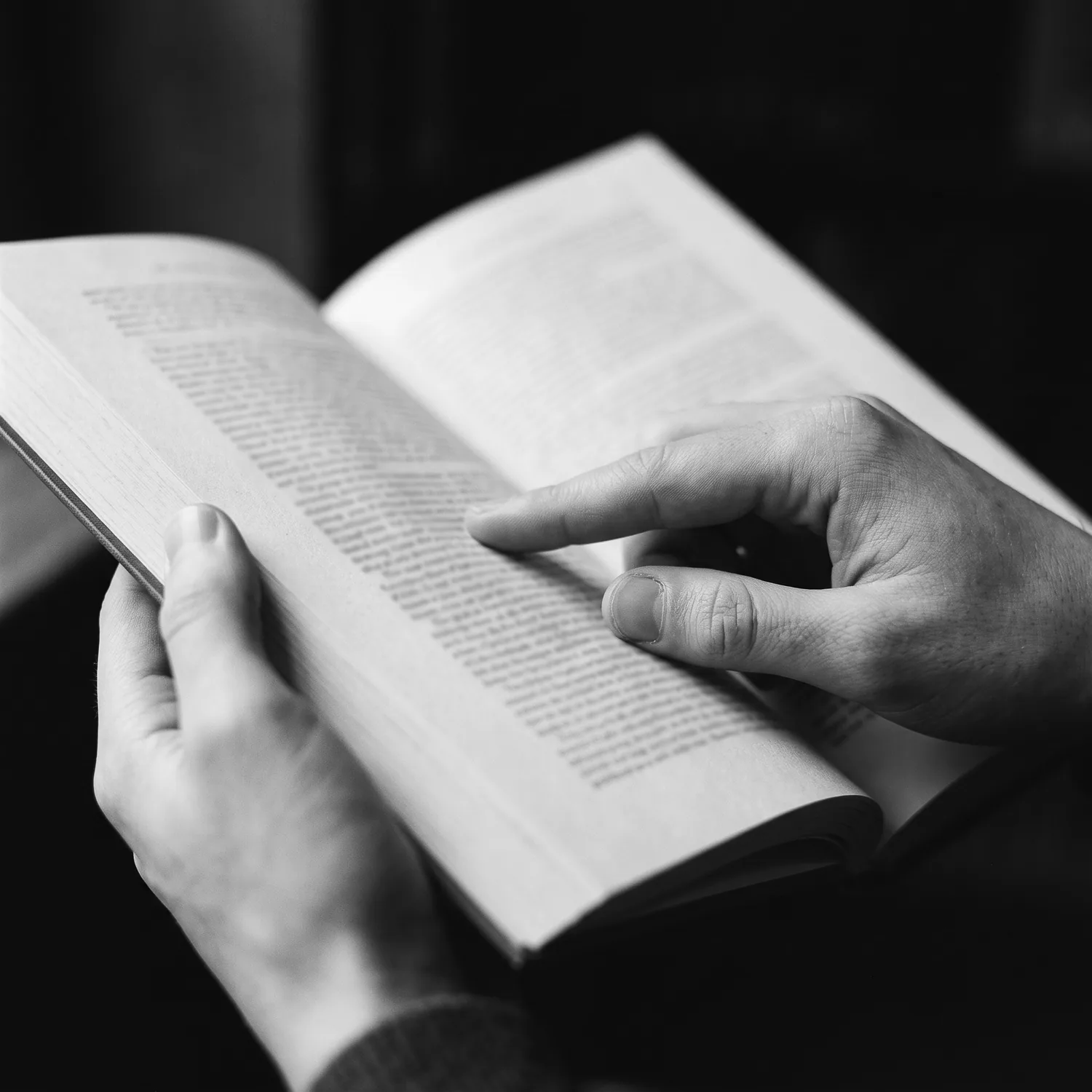Mãos segurando um livro aberto, em preto e branco